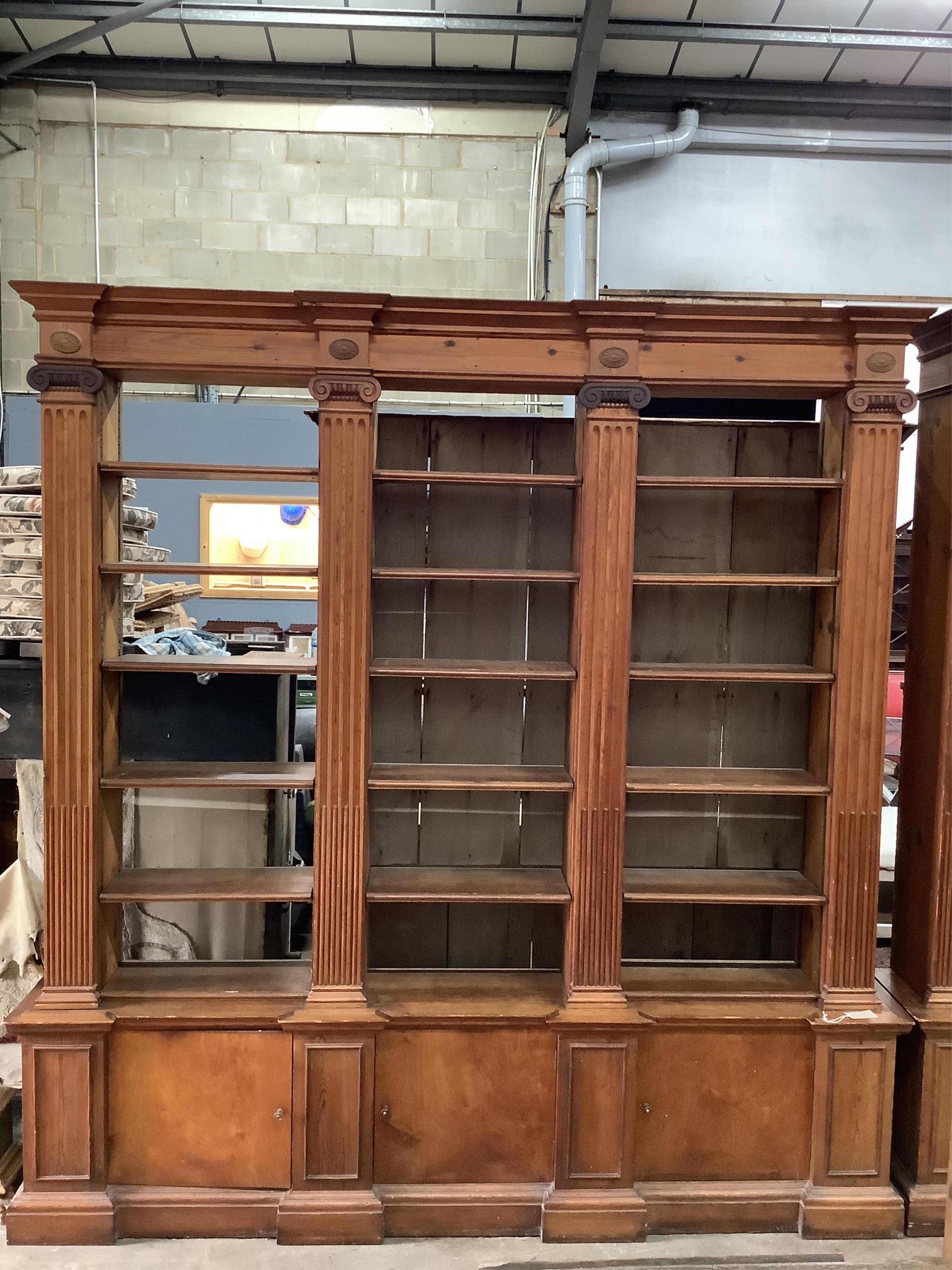 A pair of mid 20th century Sheraton style pitch pine and ply open bookcases, the adjustable shelves divided by fluted Ionic columns, each width 214cm, depth 33cm, height 222cm